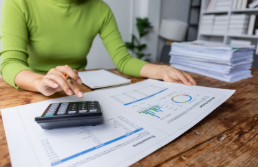 Frau sitzt am Schreibtisch und tippt auf Taschenrechner 