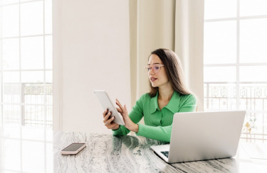 Frau sitzt am Schreibtisch und tippt auf Smartphone 